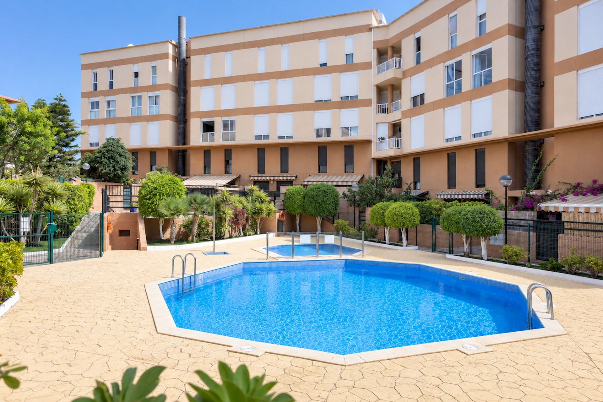 A swimming pool surrounded by a landscaped area with a multi-story building in the background.
