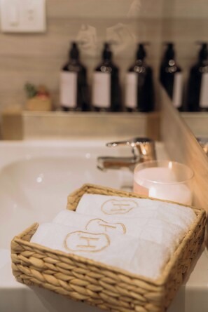 A bathroom with a white sink, a wooden basket with towels, and bottles of toiletries on a shelf. - Hazelspaces in New Cairo (New Cairo)