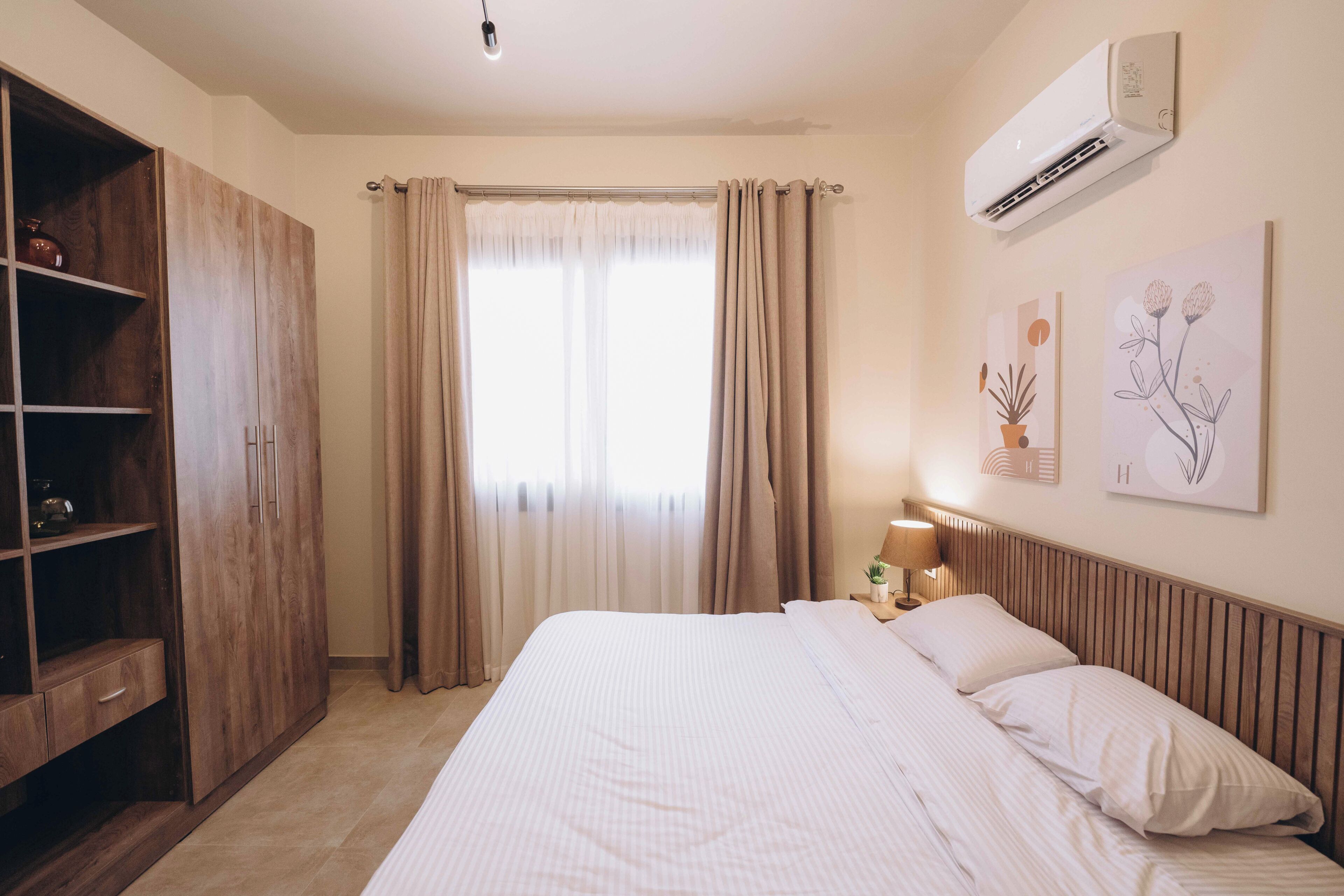 Hotelkamer met een bed, een kledingkast, een raam met gordijnen, een airconditioner en wanddecoratie.