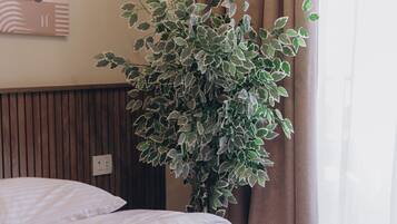 A bed with white bedding, a potted plant with variegated leaves, a wooden headboard, and a wall with a painting.