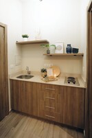 A compact kitchen with wooden cabinets, a sink, a stove, and a small shelf with decorative items.