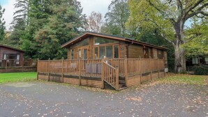 A wooden cabin with a porch, surrounded by trees and a grassy area. - 5 Waterside Wood (Windermere)