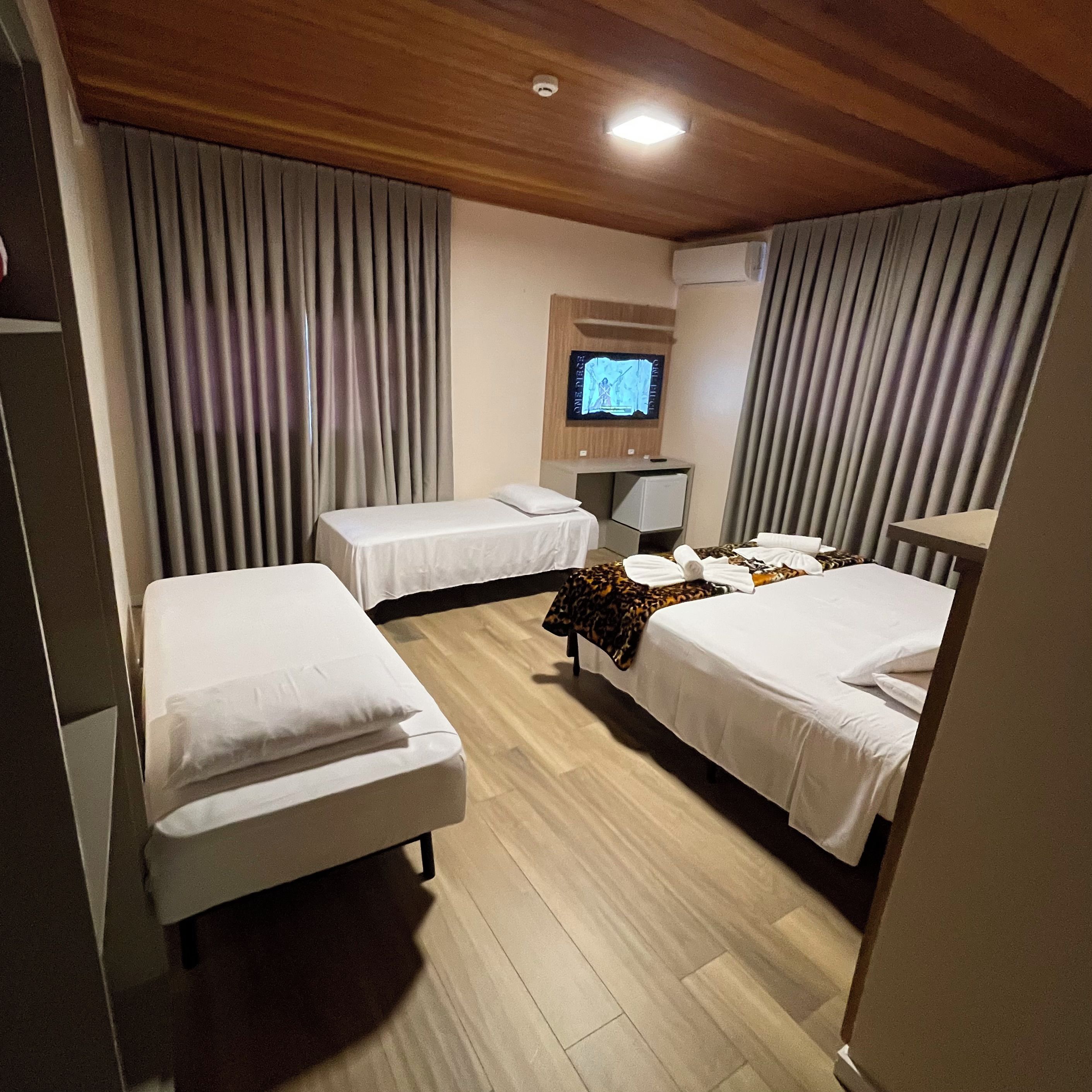 A hotel room with two single beds, a TV on the wall, and a wooden ceiling.