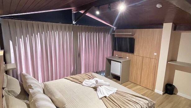 A modern bedroom with a large bed, a small desk, a TV, and a wardrobe.