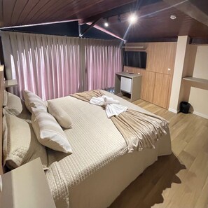 Une chambre moderne avec un grand lit, un petit bureau, une télévision et une armoire.