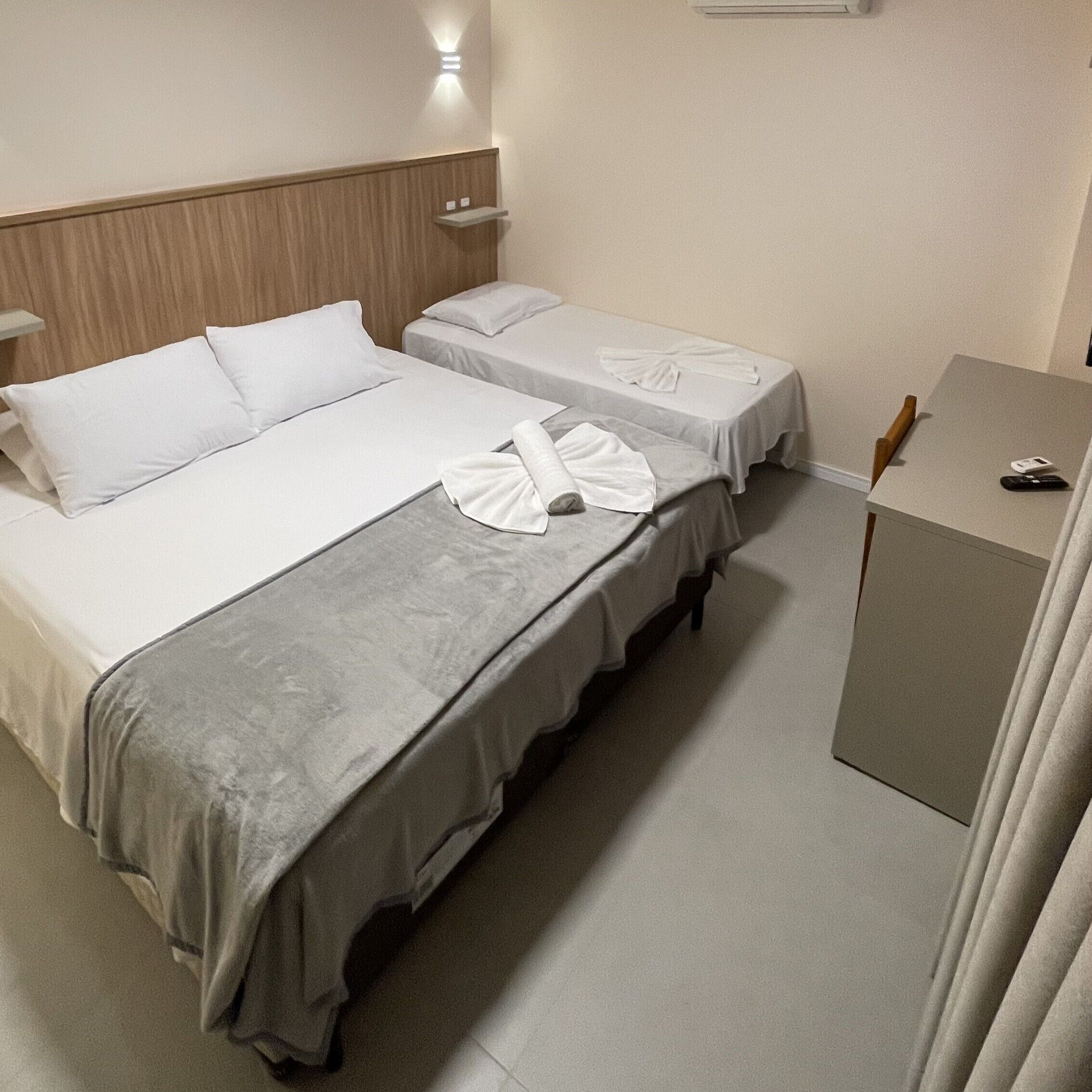 A hotel room with two beds, a bedside table, a desk, and a wall-mounted air conditioner.