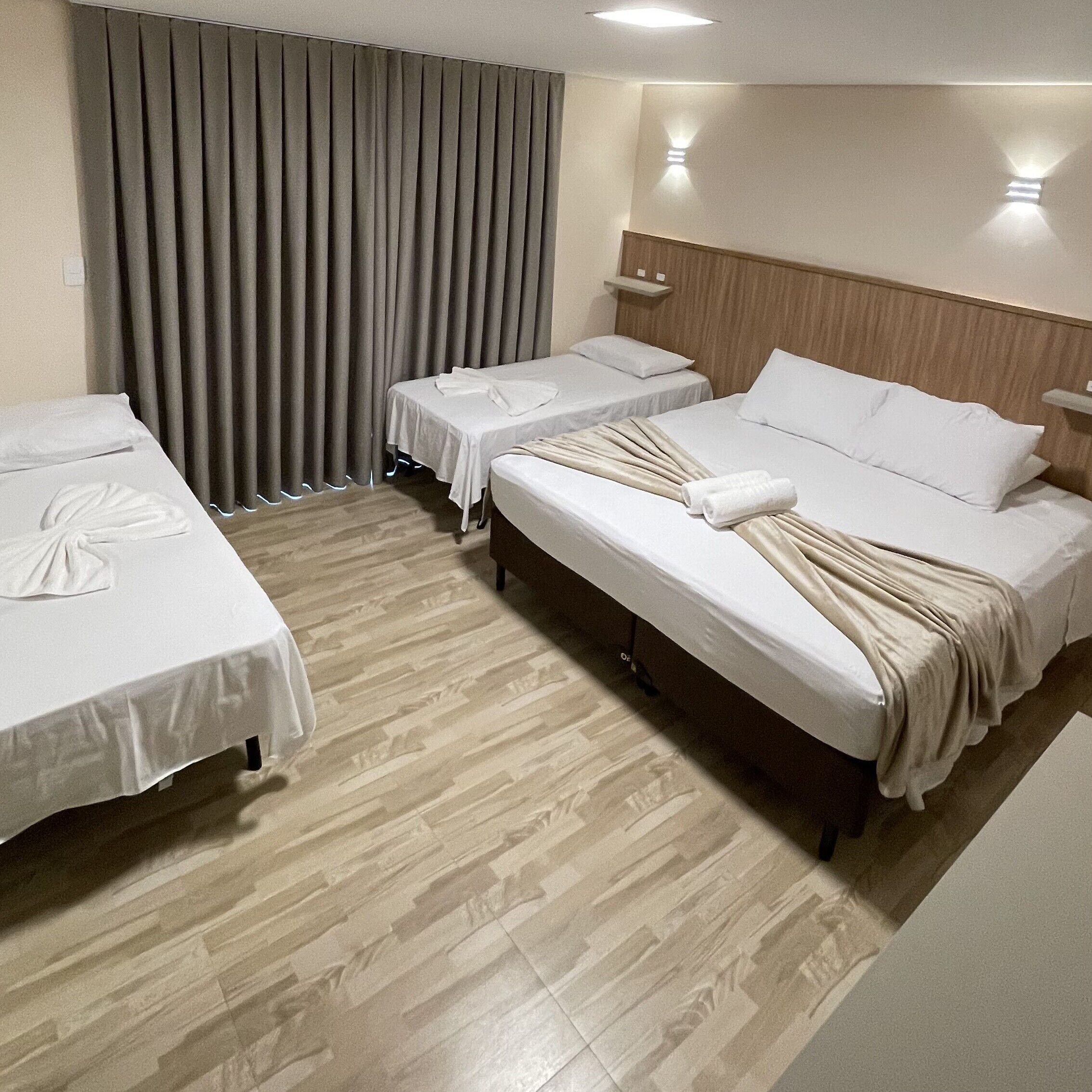 A hotel room with two single beds, a double bed, and a large window with curtains.