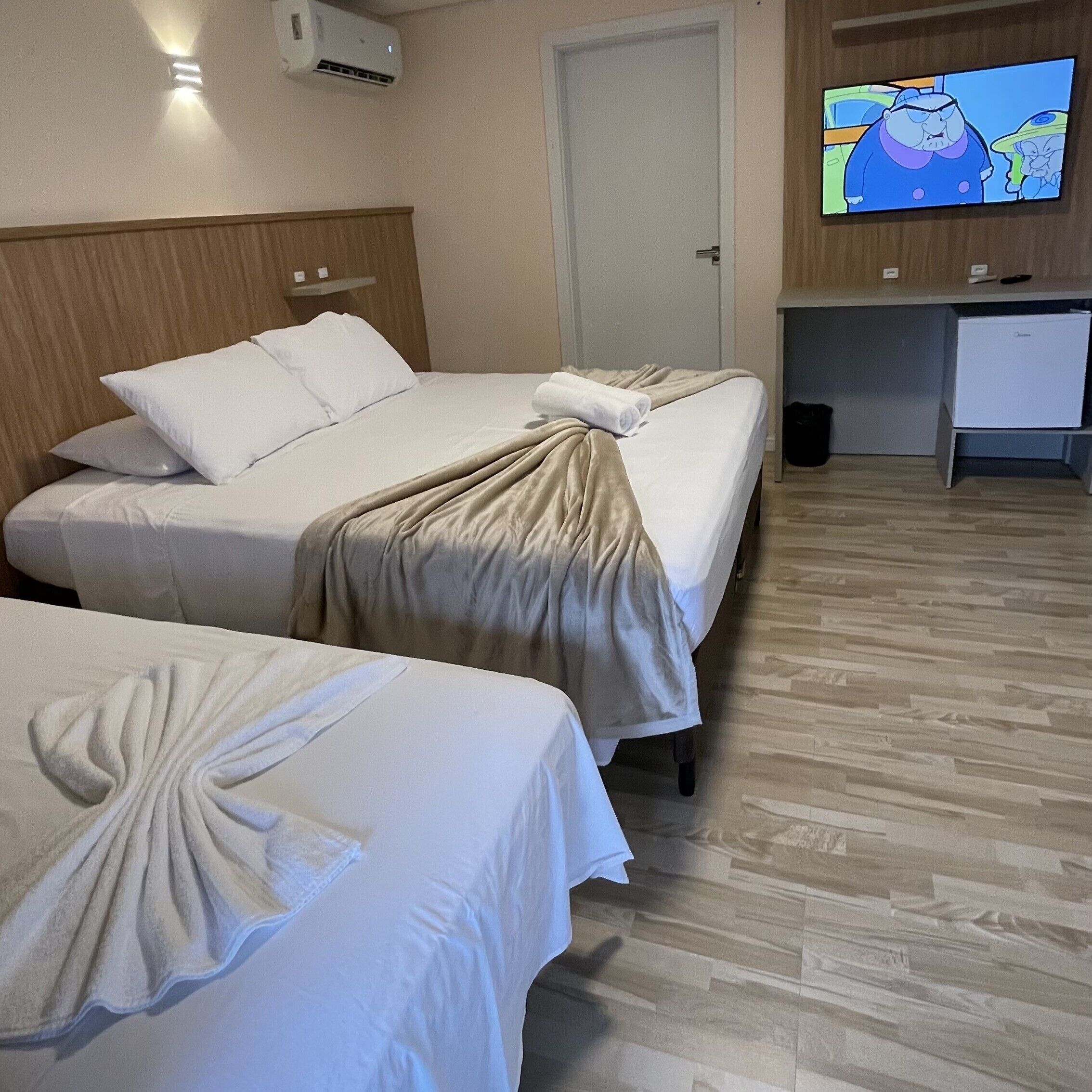 Ein Hotelzimmer mit zwei Betten, einem Schreibtisch, einem Fernseher und einer Klimaanlage.