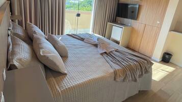 A modern bedroom with a large bed, curtains, a TV, and a small kitchenette.