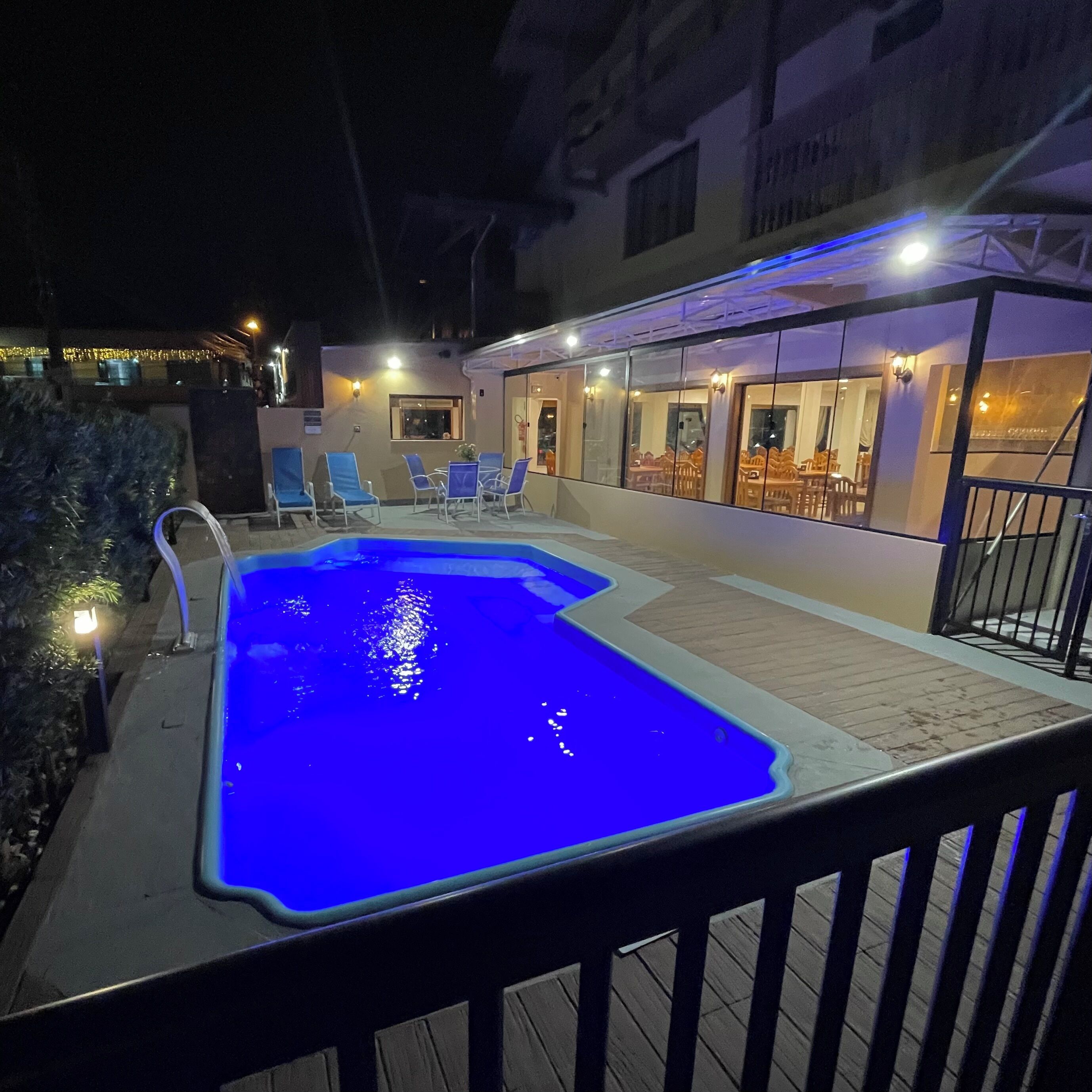 Una piscina con tonalidades azules, rodeada por una terraza con sillas y una zona de estar cubierta.