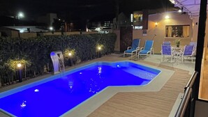 A swimming pool with a wooden deck, surrounded by lounge chairs and a small building with a sign that reads "DALLAS".