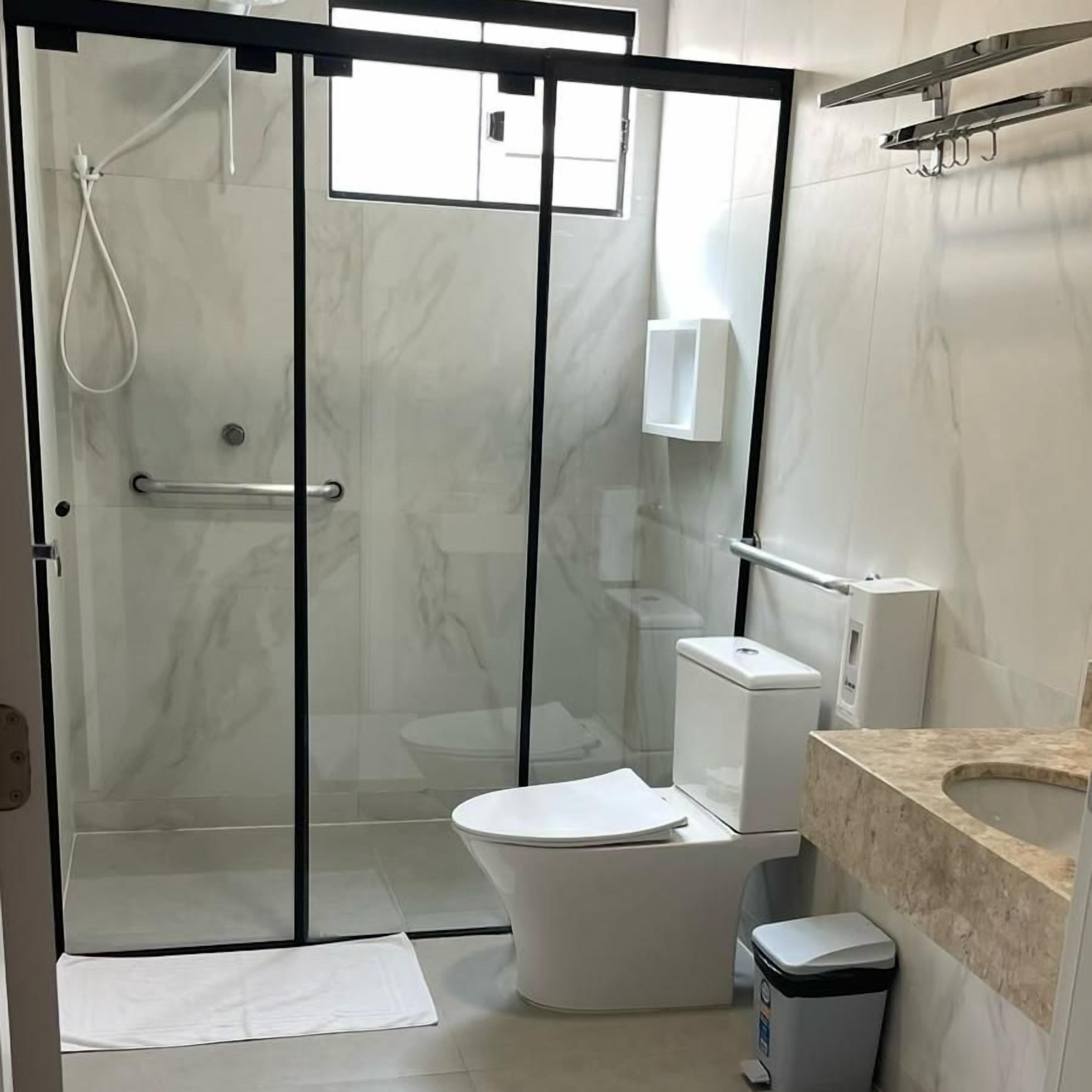 A modern bathroom with a glass-enclosed shower, a toilet, a sink, and a trash bin.