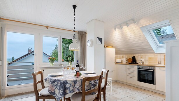 A kitchen with a dining table set for four, a clock, and a window overlooking a balcony. - Apartment 'Holiday Apartment, 60 sqm' with Balcony and Wi-Fi (Ammerbuch)
