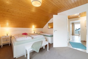 Ein Schlafzimmer mit schrägverdeckter Decke, einem Bett mit Sitzbank, Nachttischen und einer Tür zu einem anderen Raum.