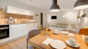 A modern kitchen with white cabinets, a dining table set with plates, cups, and a bowl of muffins. - Studio Apartment, 32 sqm, with Wi-Fi (Ammerbuch)