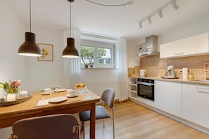 A modern kitchen with white cabinets, a wooden countertop, and a dining area with a table set for two. - Studio Apartment, 32 sqm, with Wi-Fi (Ammerbuch)