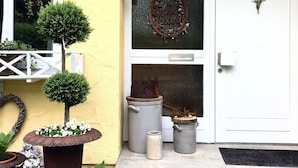 A yellow building with a white door, a metal bullhead, a wreath, and potted plants. - Studio Apartment, 32 sqm, with Wi-Fi (Ammerbuch)