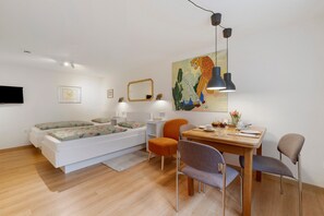 A modern room with a bed, a dining table with chairs, a painting, and a TV mounted on the wall. - Studio Apartment, 32 sqm, with Wi-Fi (Ammerbuch)