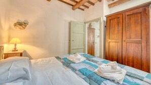 A bedroom with a bed, a nightstand with a lamp, a wooden wardrobe, and a green door. - GuestHost - Lovely Apartment in the Perugian Hills (Bagnaia)