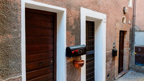 A narrow alley with a rustic building, a wooden door, a mailbox, and a small window with a number. - GuestHost - Lovely Apartment in the Perugian Hills (Bagnaia)