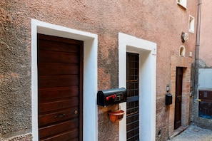 Un estrecho callejón con un edificio rústico, una puerta de madera, un buzón y una pequeña ventana con un número.