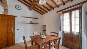 A dining area with a wooden table and chairs, a clock on the wall, and a window with lace curtains. - GuestHost - Lovely Apartment in the Perugian Hills (Bagnaia)