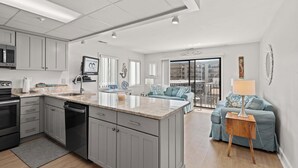 A modern kitchen with grey cabinets, a central island, and a dining area with a blue sofa and a wooden side table. - Silver Sun 201 (Ocean City)