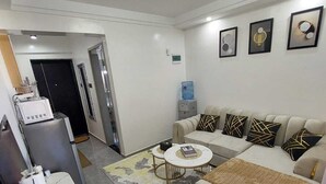 A modern living room with a sofa, coffee table, and a small kitchen area with a refrigerator and microwave.