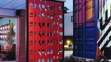 A modern outdoor seating area with a red partition, a blue shipping container, and a glass door entrance.