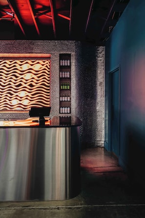 Un espace d’accueil au design moderne, comprenant un mur décoré de motifs, un comptoir et une étagère où sont exposées des bouteilles.