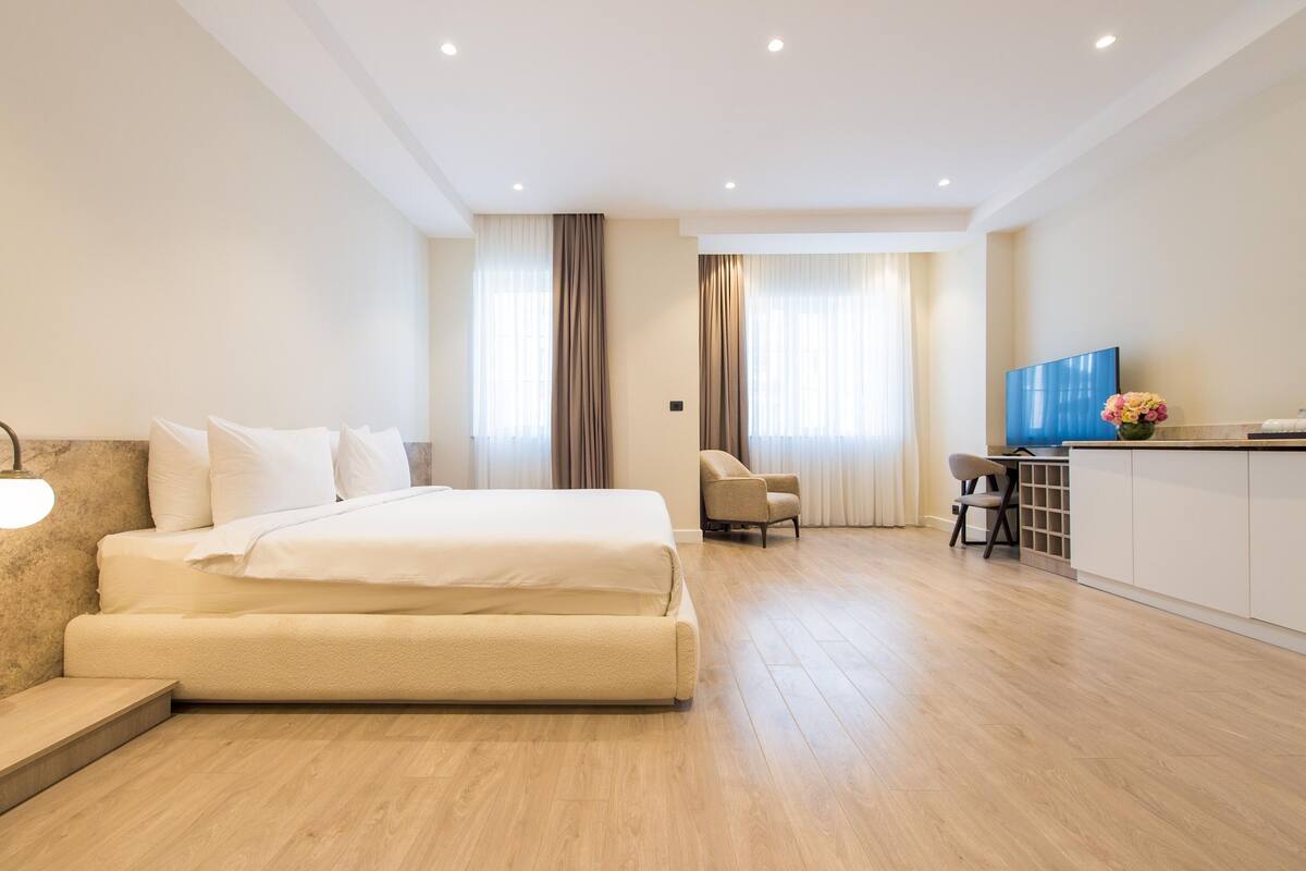 Ein modernes Hotelzimmer mit einem großen Bett, einem Schreibtisch mit Flachbildfernseher und einer Sitzecke mit zwei Sesseln.