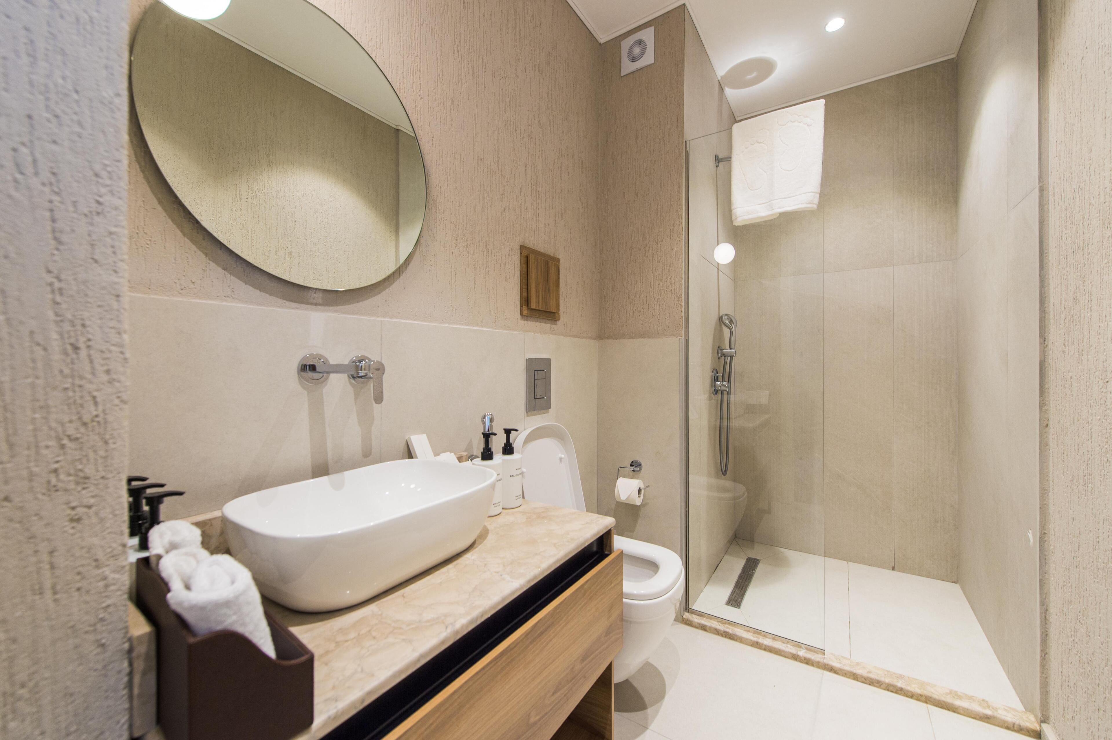 A modern bathroom with a large oval sink, a toilet, and a glass-enclosed shower.