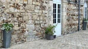 A stone building with a cobblestone courtyard, a white door, and flower planters. - La ferme de Valeuse (Morienval)