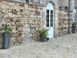Um edifício de pedra com um pátio de paralelepípedos, uma porta branca e vasos de flores.