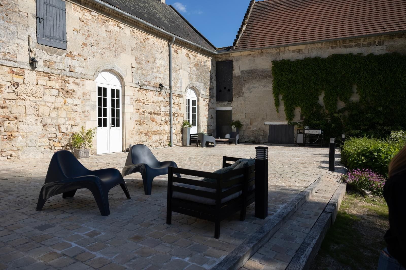An outdoor seating area with stone walls, a grill, and potted plants.