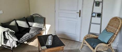 A room with a sofa, a small table, a wicker chair, a white door, and a ladder against the wall.
