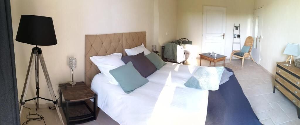 A hotel room with a bed, bedside table, lamp, chair, and a dresser.