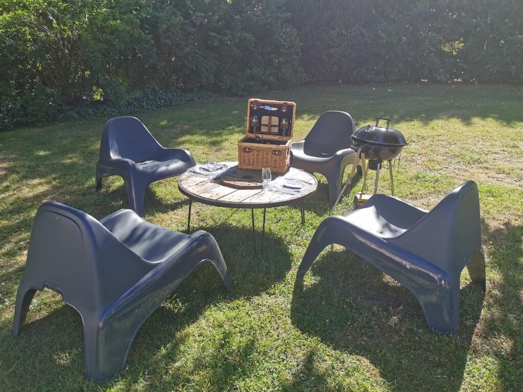 Ein runder Tisch mit vier Stühlen, einem Korb und einem Grill in einer grünen Außenanlage.