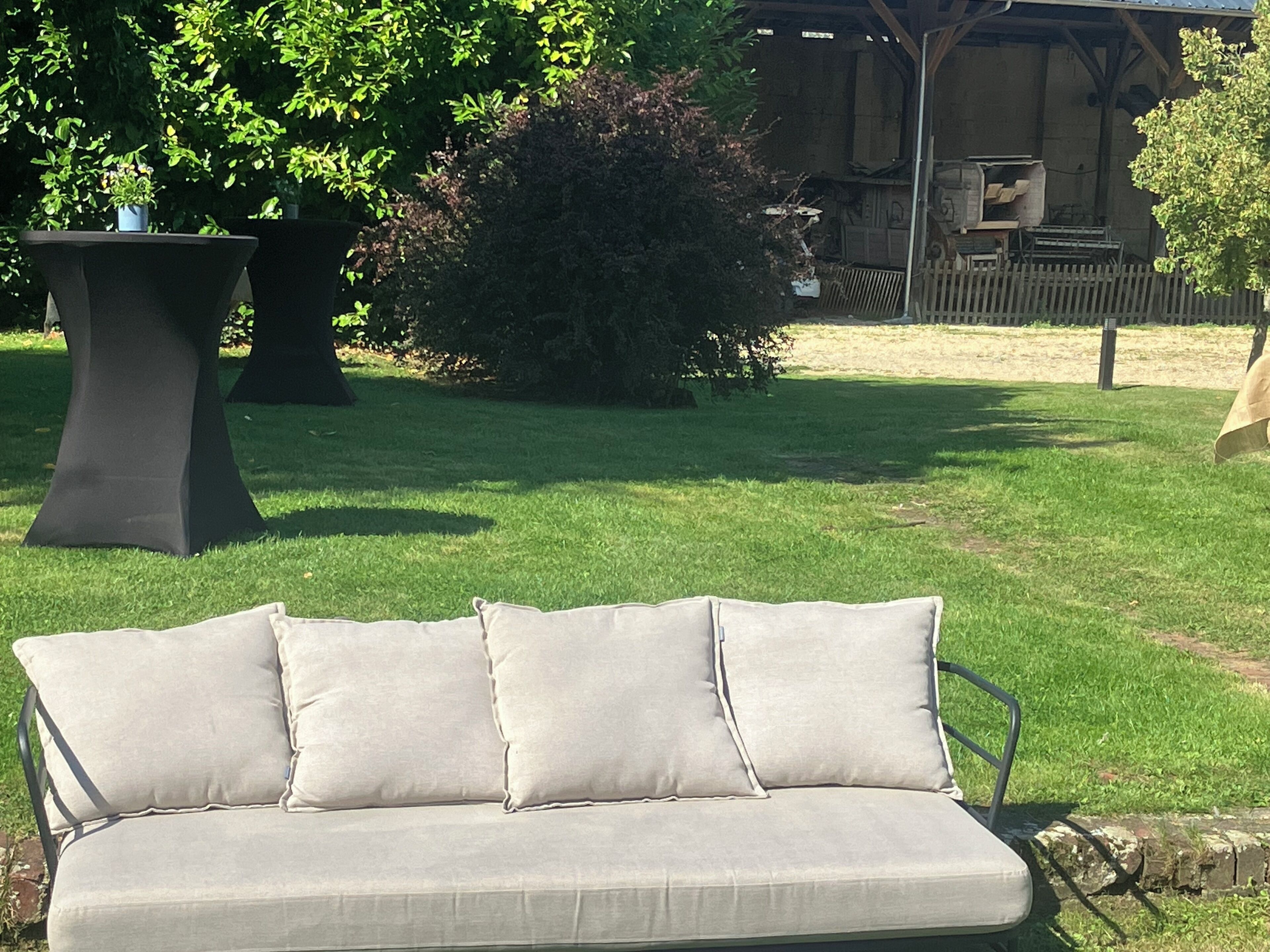 Un canapé d’extérieur de couleur beige, doté de coussins, placé sur une pelouse verdoyante.