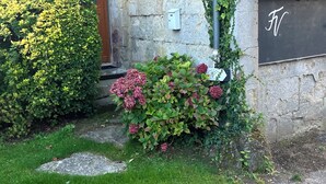 A stone building with a wooden door, a mailbox, and a small garden with green shrubs and pink flowers. - La ferme de Valeuse (Morienval)