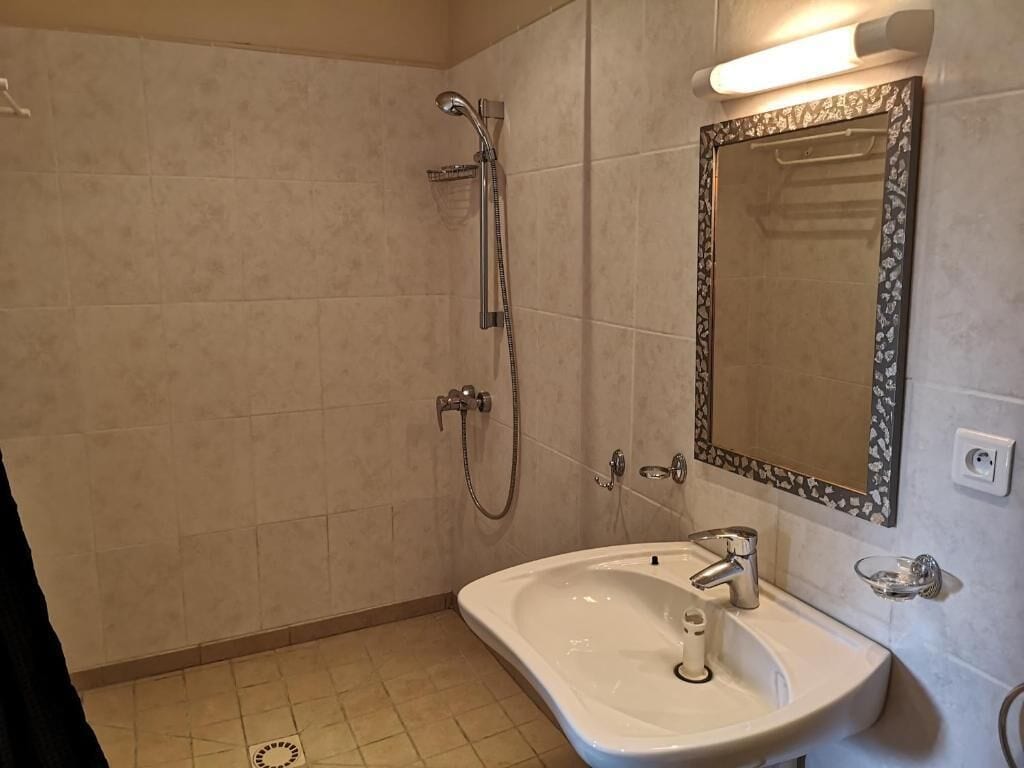 Une salle de bain avec un lavabo, un miroir, une douche et des murs carrelés.
