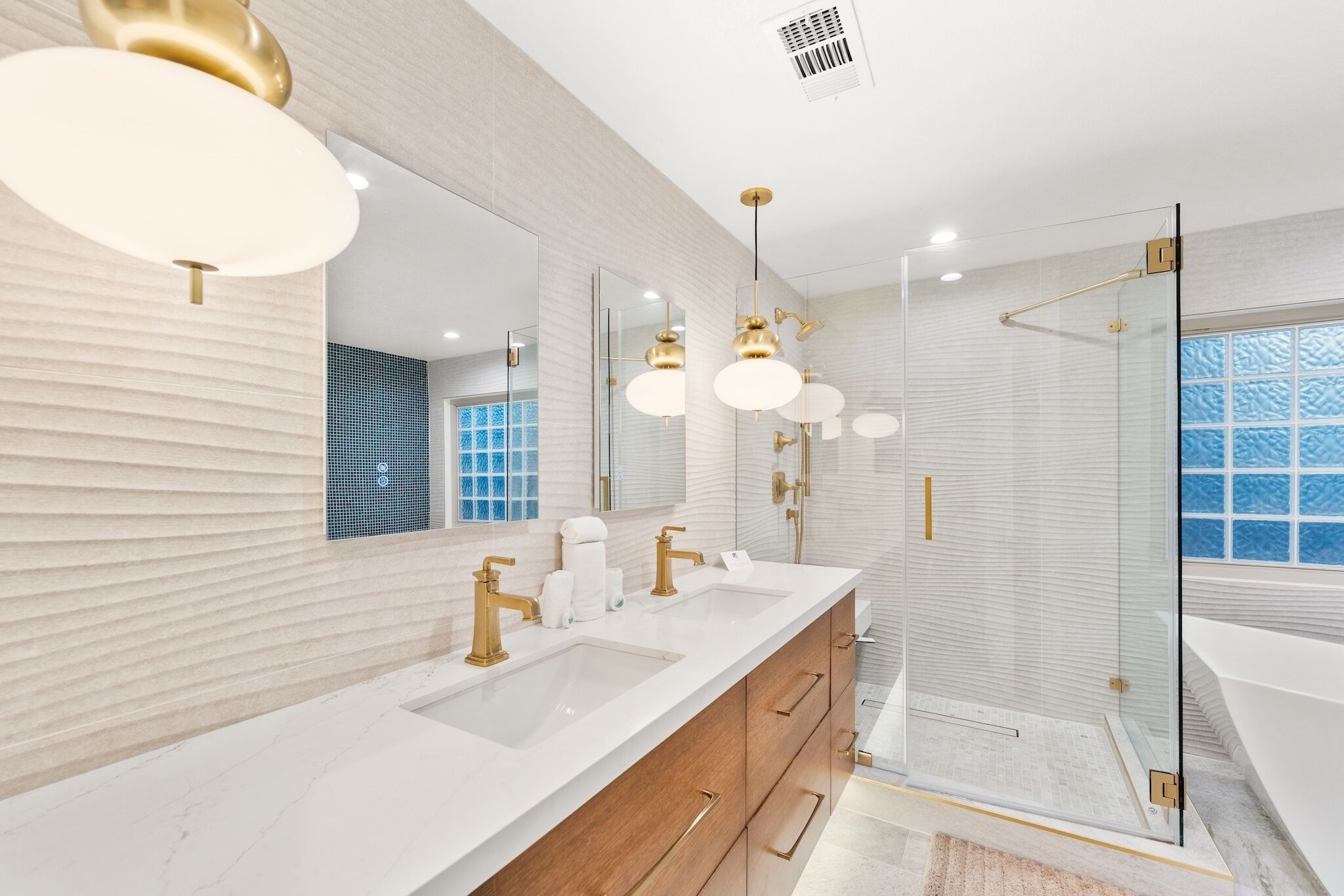 A modern bathroom with two sinks, a large mirror, and a glass-enclosed shower.