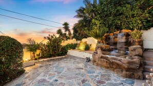 Une terrasse en pierre agrémentée d’une cascade, entourée d’une végétation luxuriante et de palmiers.