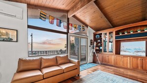 Un salon moderne avec un canapé en cuir, de grandes fenêtres, un plafond en bois et une vue sur le coucher de soleil.