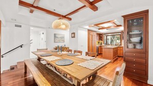 Un grand espace à manger avec une table et des bancs en bois, une cuisine dotée de meubles en bois et un escalier menant à un autre niveau.