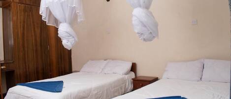 A hotel room with two beds, wooden wardrobe, and a wall-mounted light fixture.