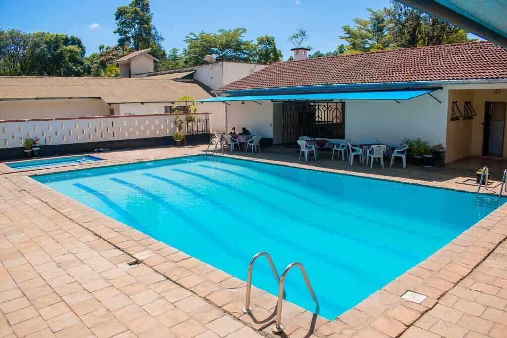 A swimming pool with a clear blue water, surrounded by a tiled patio area with chairs and tables.