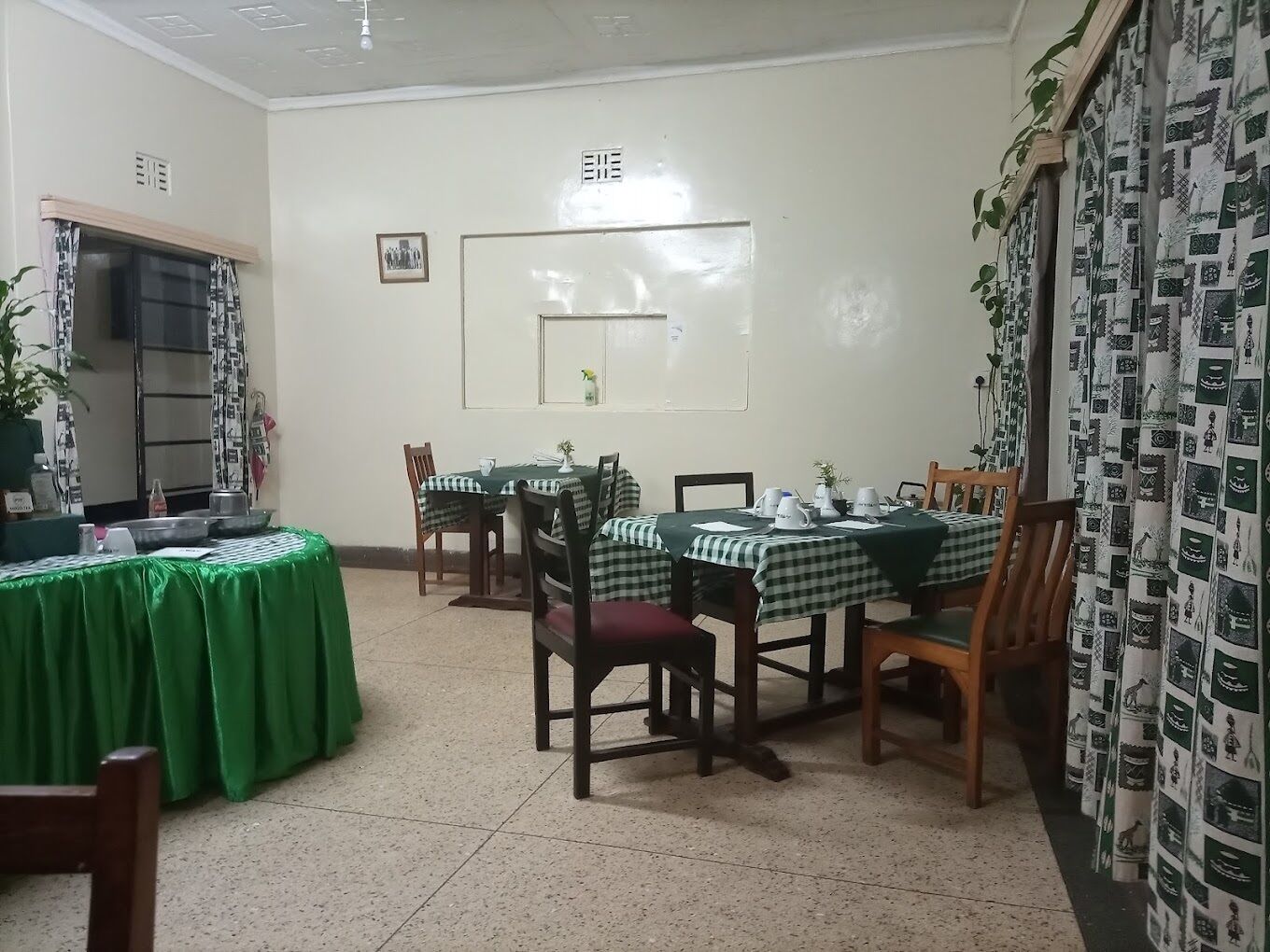 Ruokailutila, jossa on ruutukuosiset pöytäliinat, puiset tuolit ja vihreällä pöytäliinalla peitetty pöytä.