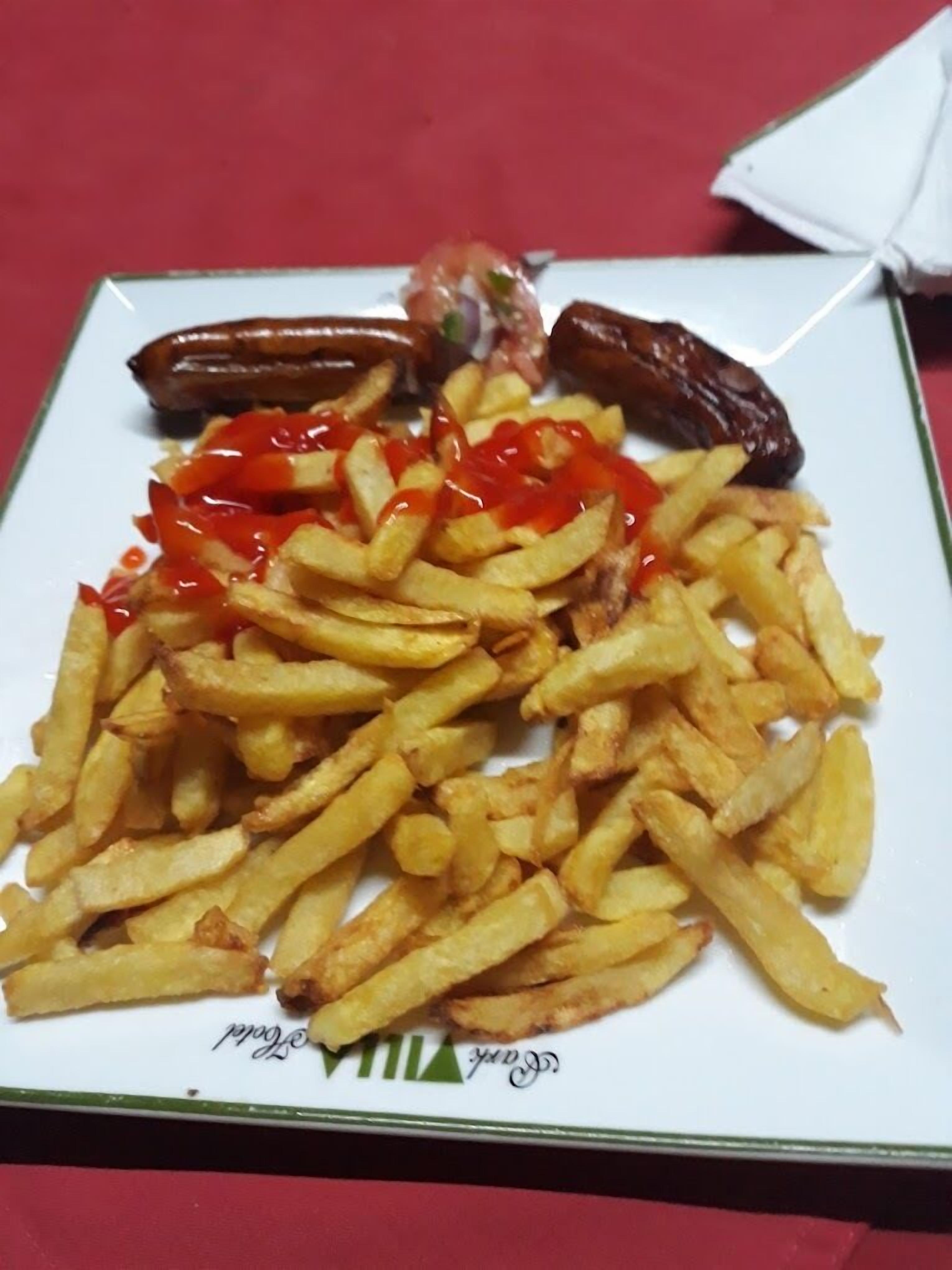 Un plato de comida con papas fritas, salchichas y una pequeña ensalada.