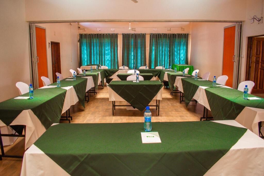 Ein Konferenzraum mit mehreren Tischen, jeweils mit einer grünen Tischdecke, weißen Stühlen und Wasserflaschen.